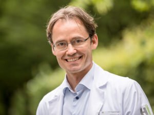 Dr. med. Marc Schlaeppi in weisser Kleidung vor grünem Blattwerk