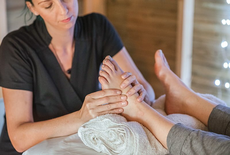 Frau führt Massage an linkem Fuss einer liegenden Person aus