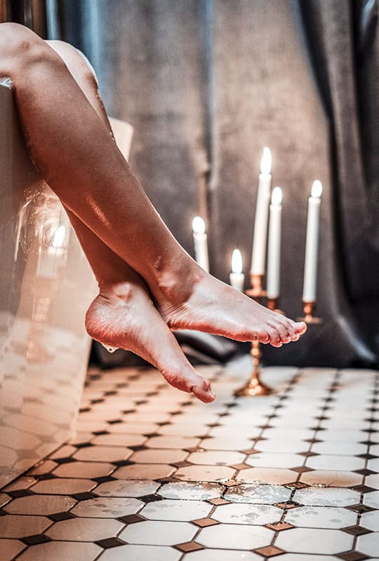 nasse Unterschenkel von auf Badewannenrand sitzender Frau mit Kerzenlicht