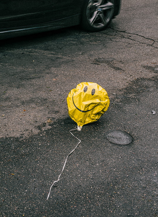 Halb entlüfteter Luftballon mit Smiley-Motiv liegt auf Fahrbahn