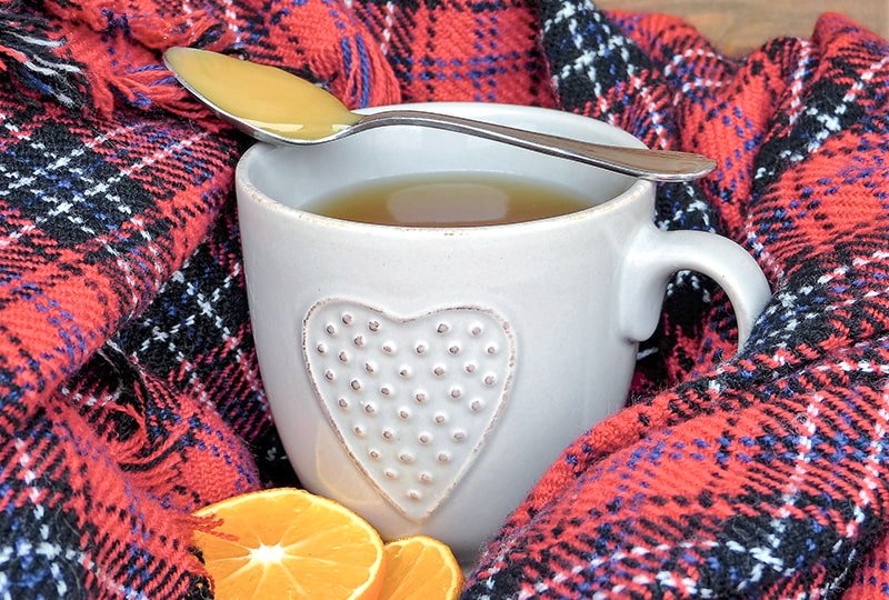 Becher mit Tee und Honiglöffel auf Wolldecke
