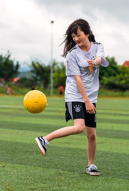 Junge Frau spielt auf Rasenplatz vergnügt mit einem Fussball