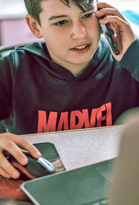 Junge tele­foniert beim Arbeiten mit der Maus am Laptop