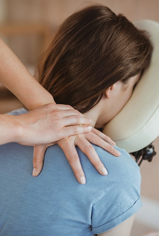 Junge Frau mit dem Kopf im Polster eines Massage-Stuhls wird an der Schulter massiert