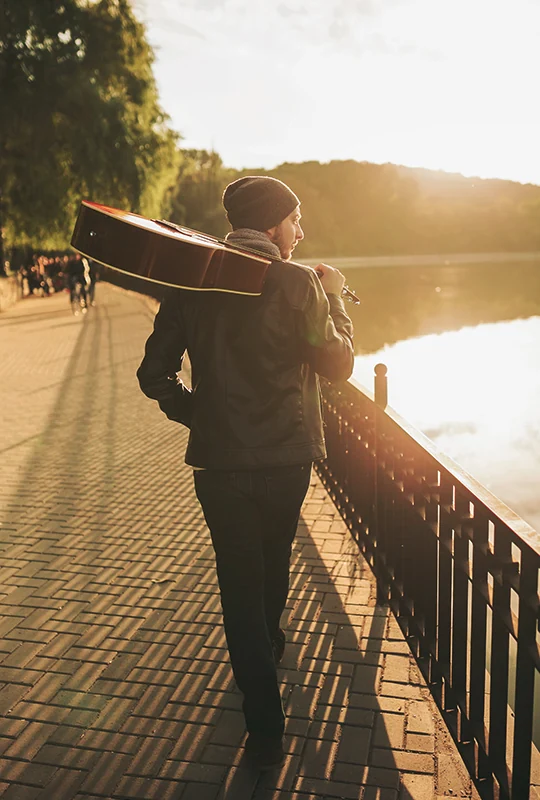 Junger Mann mit Gitarre auf der Schulter läuft einem Fluss entlang