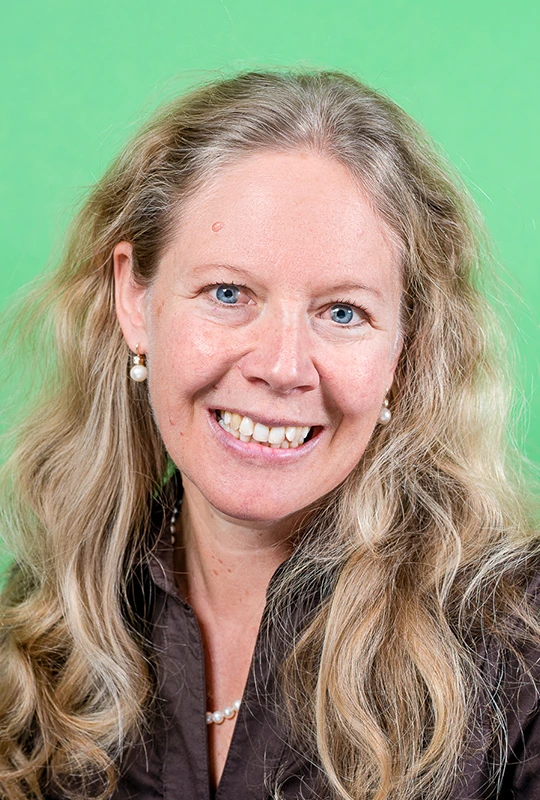 Portrait von lächelnder Frau mit langem blondem Haar vor grünem Hintergrund