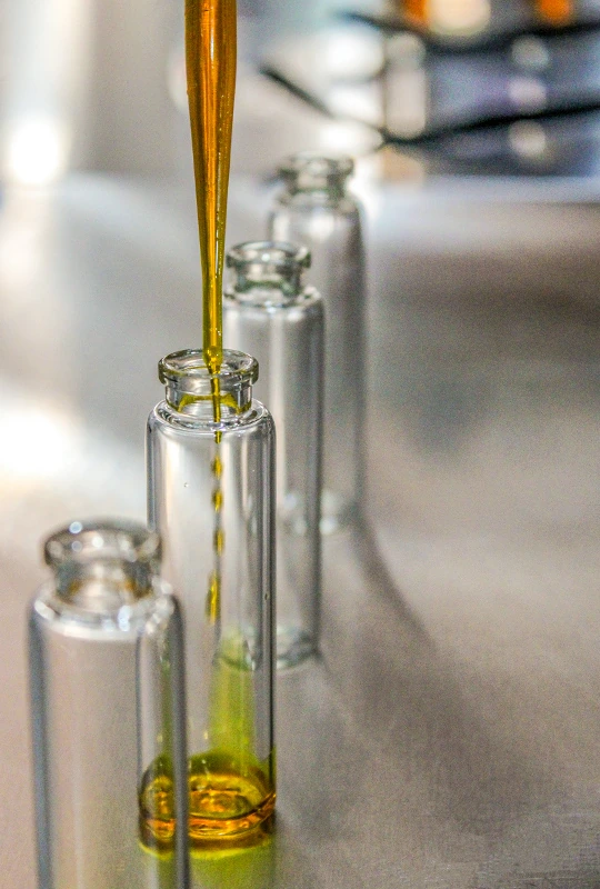 Les flacons en verre sont remplis d'huile végétale à l'aide d'une pipette.