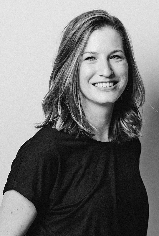 Schwarzweiss-Foto einer jungen, lächelnden Drogistin in schwarzem T-Shirt