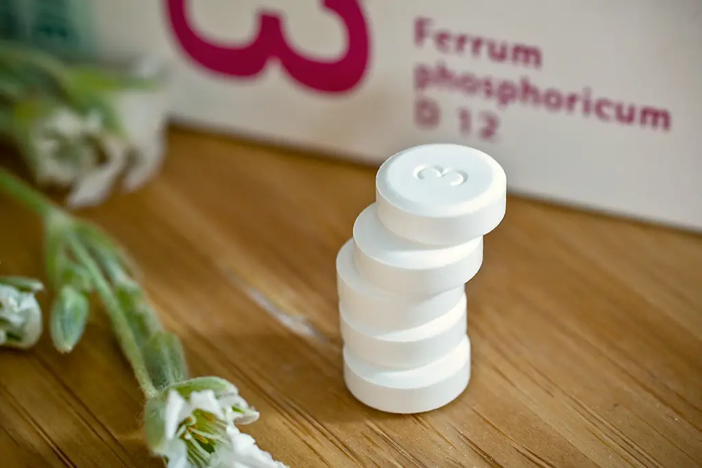 Ein Stapel von fünf weissen Schüssler Salz Tabletten liegen neben der Packung auf einer hölzernen Unterlage