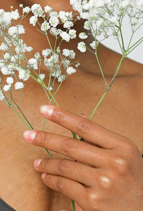 Eine Hand hält eine Blume vor Hals und Schulter