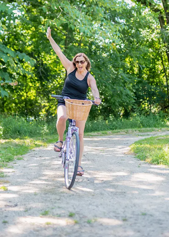 Eine sommerlich gekleidete Frau fährt jubelnd mit einer Hand in der Luft Fahrrad