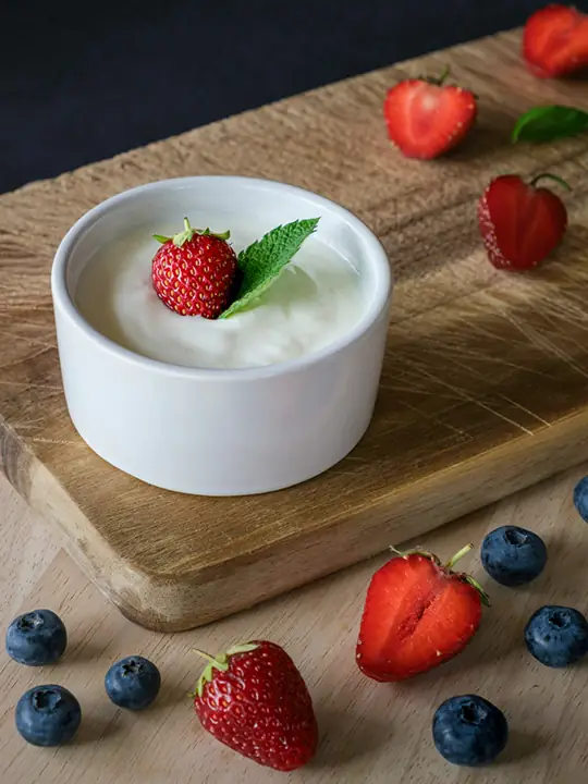 Eine kleine, mit Joghurt gefüllte Keramikschale ist von Früchten umgeben