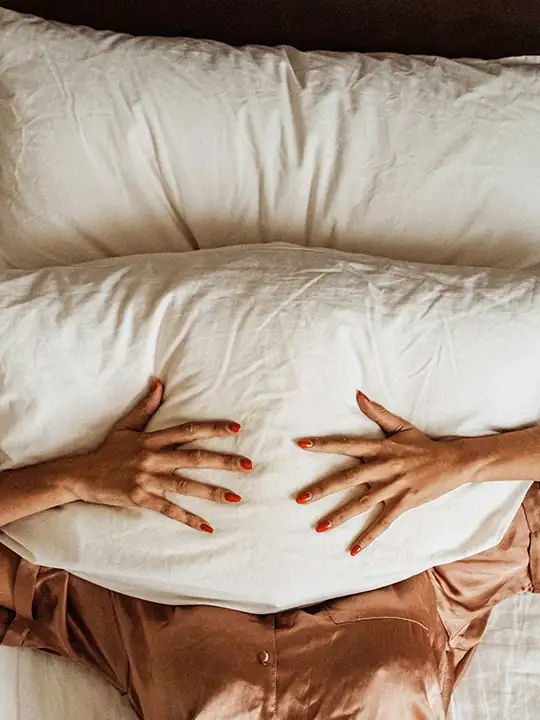 Auf dem Rücken im Bett liegende Person hält ein Kissen über das Gesicht