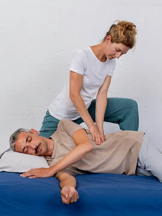 Shiatsu-Therapeutin behandelt einen auf der Seite liegenden Mann